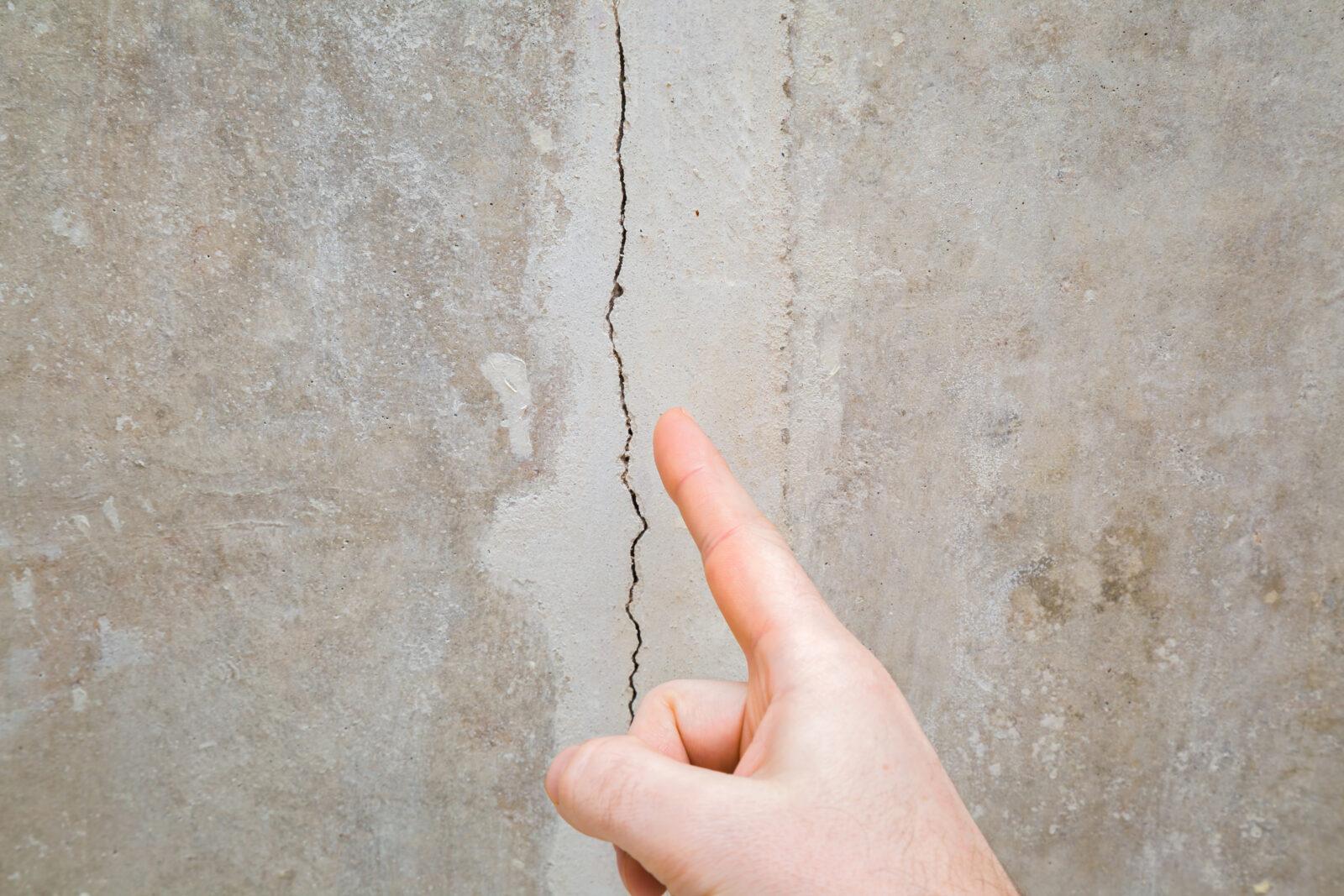 A finger pointing to a vertical crack in a concrete wall