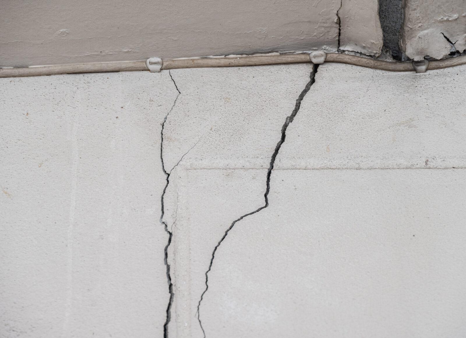 Close-up photo of a vertical crack running down a painted concrete foundation wall